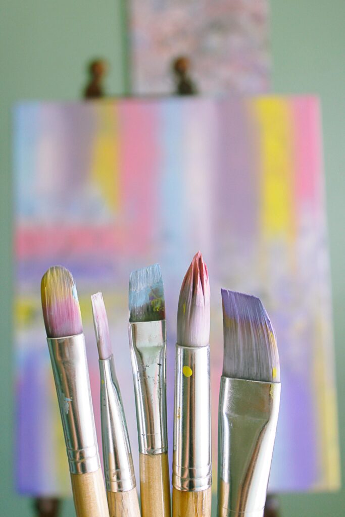Paintbrushes in front of a colorful canvas.